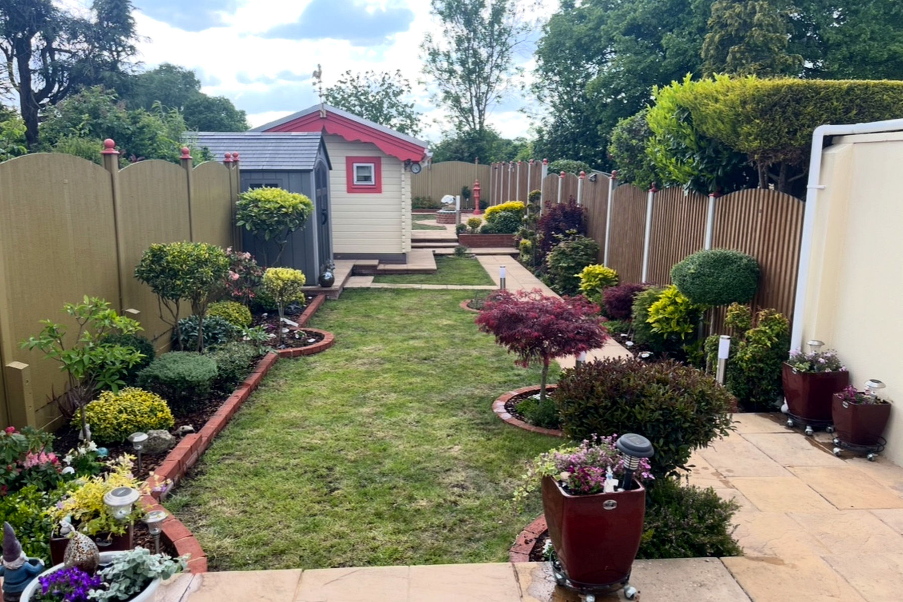 Colourful, well-tended garden borders and lawn with a Japanese maple